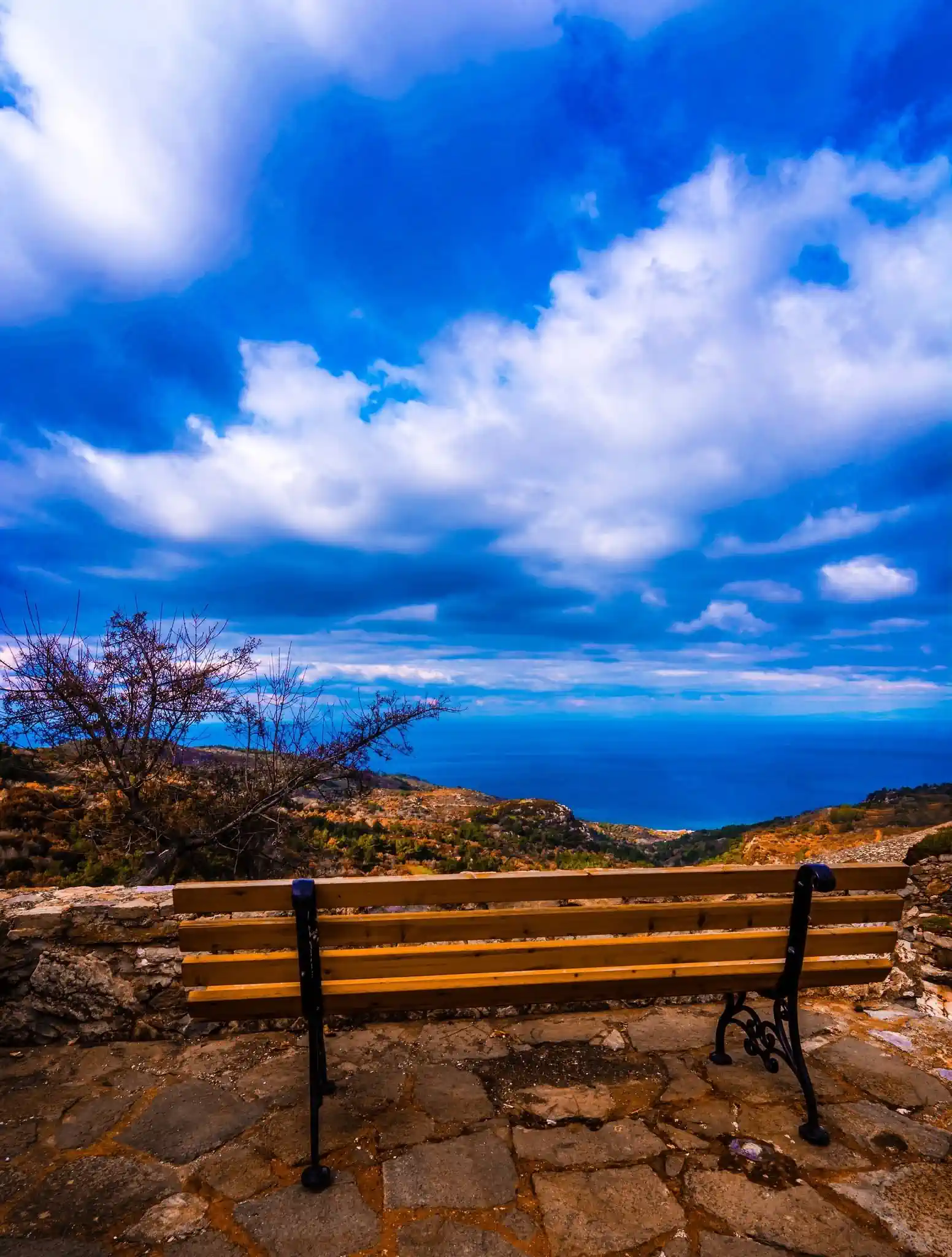 Bench overlooking the coastline and mountainous landscape of Chios under a dramatic blue sky