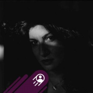 Professional portrait of Greek singer Fevronia, showing a woman with dark curly hair against a softly blurred background, Cologne