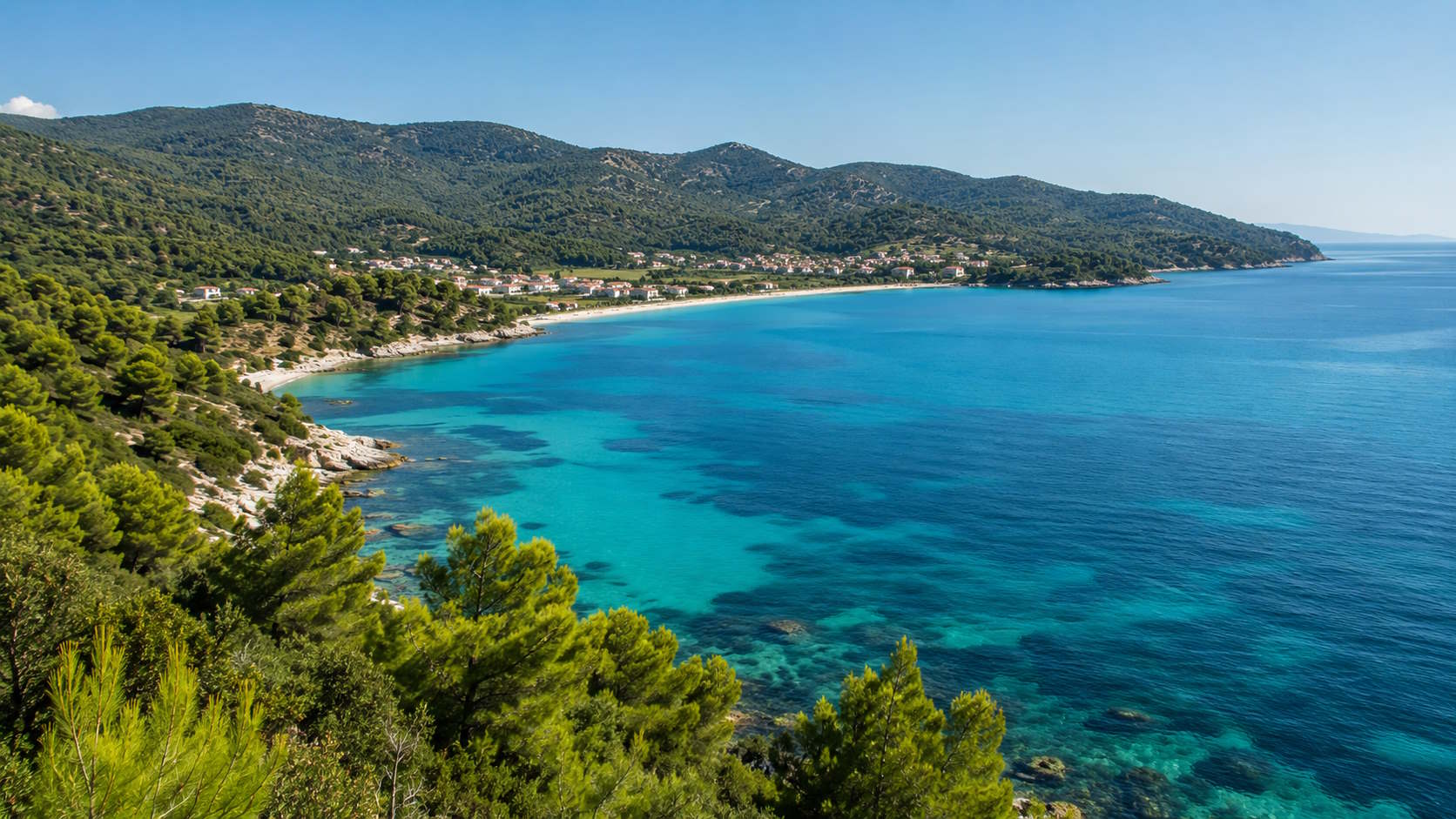 Turquoise bay, pine-covered hills and coastal village in Halkidiki, Greece