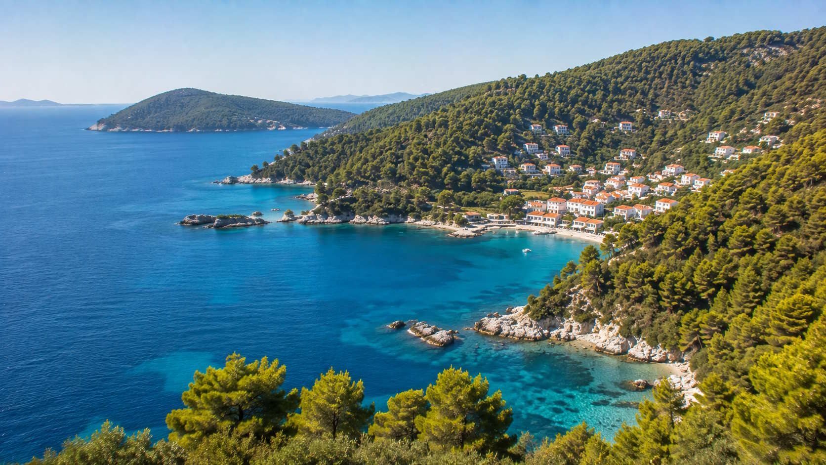 Forested Sporades coastline with turquoise Aegean waters and seaside village