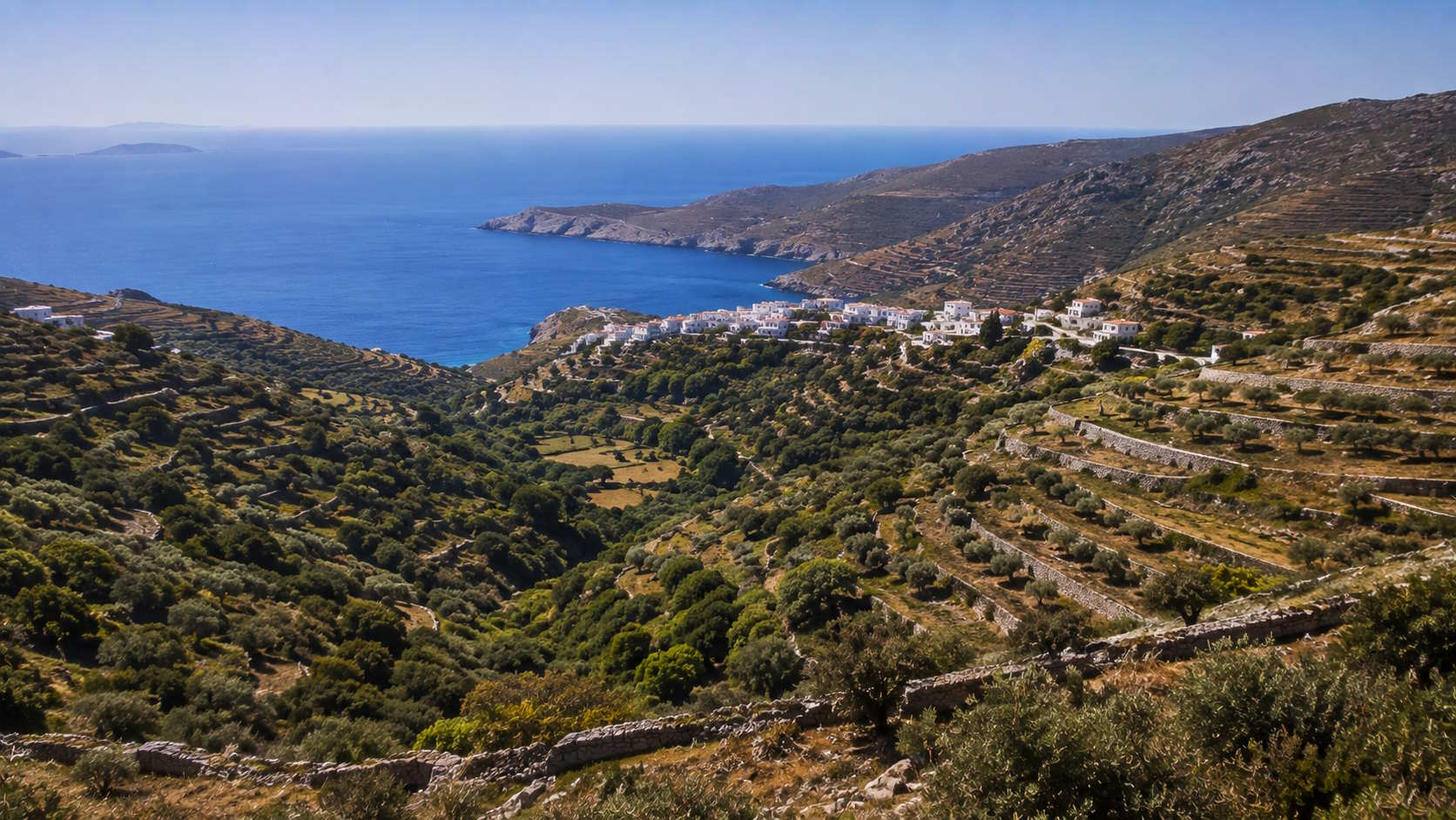 Green valley, terraced hillsides and coastal village overlooking the Aegean Sea in Andros, Greece